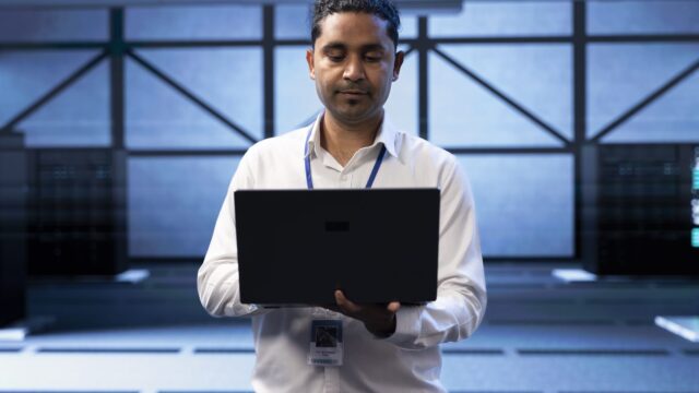 Engineer in server farm checking recovery plan on laptop monitoring data center