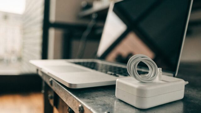 A silver laptop on a workbench next to a compact white power adapter with its cable neatly coiled