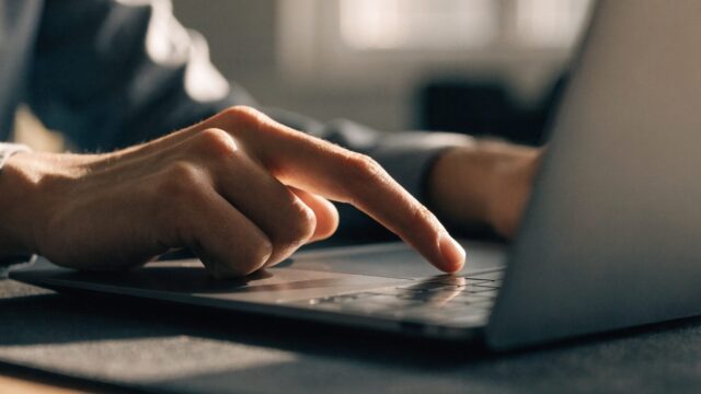 A finger gliding on the touchpad of a graphite black laptop on a dark desk mat