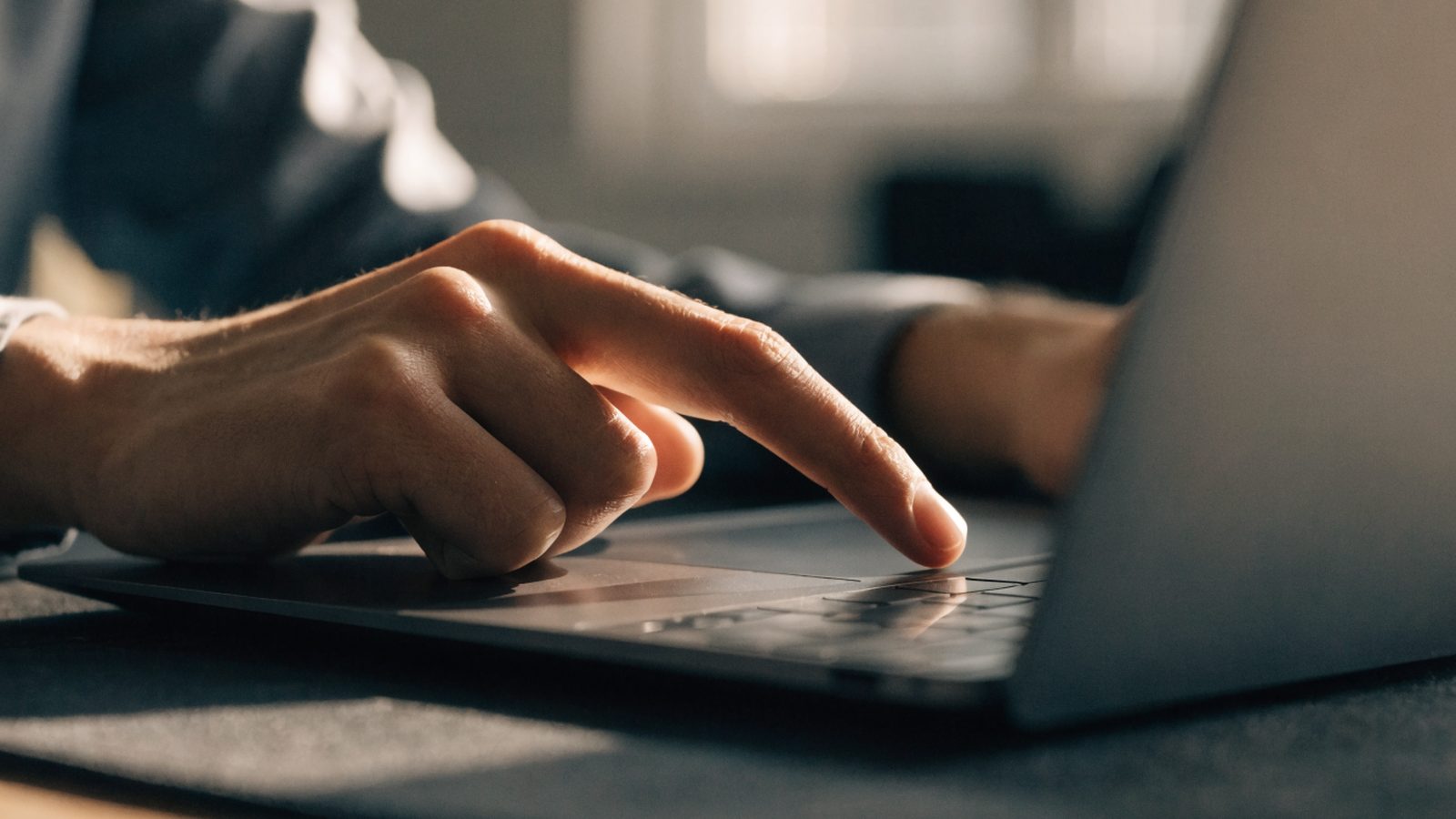 A finger gliding on the touchpad of a graphite black laptop on a dark desk mat
