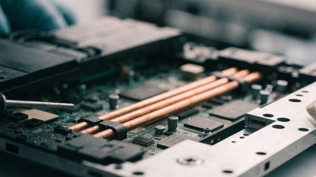 Close-up of a laptop motherboard with copper heat pipes during a repair