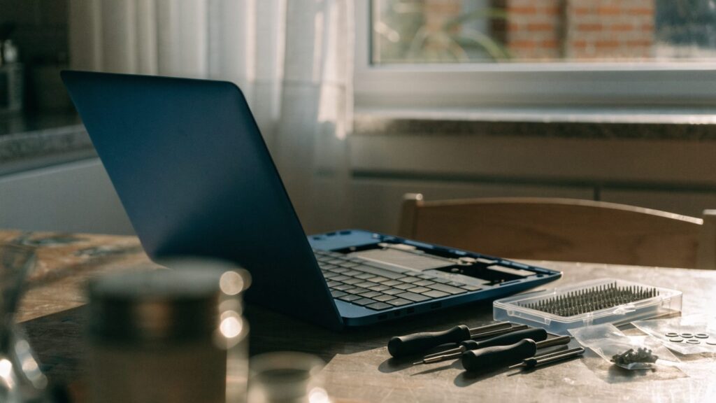 A precision screwdriver kit laid out beside a partially opened dark blue laptop on a kitchen table