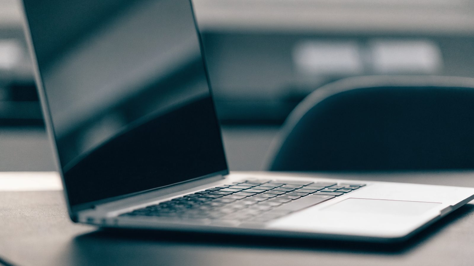 A silver laptop on a dark desk mat with a completely dark blank screen