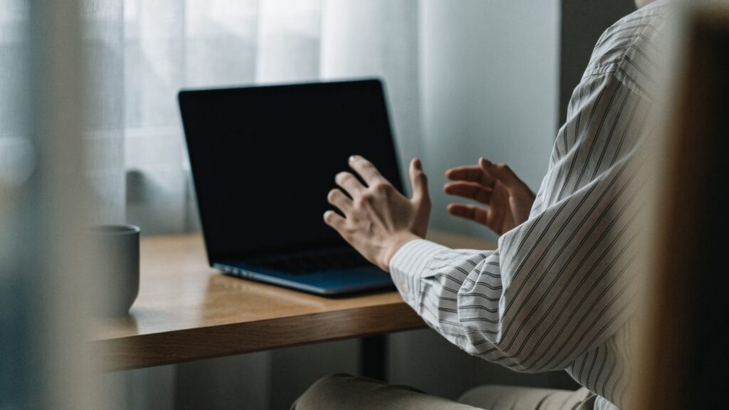A person seen from behind with hands raised at a dark blue laptop with a dark blank screen on a wooden desk
