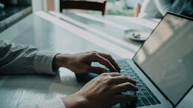 Hands typing on the keyboard of a matte grey laptop on a kitchen table