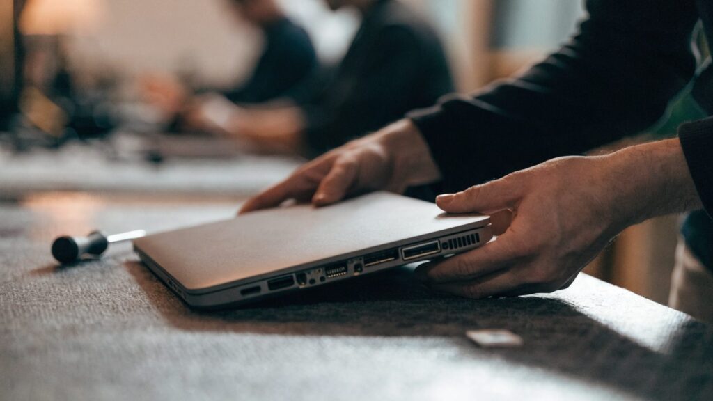 A technician lifting the bottom cover off a matte grey laptop on an anti-static mat