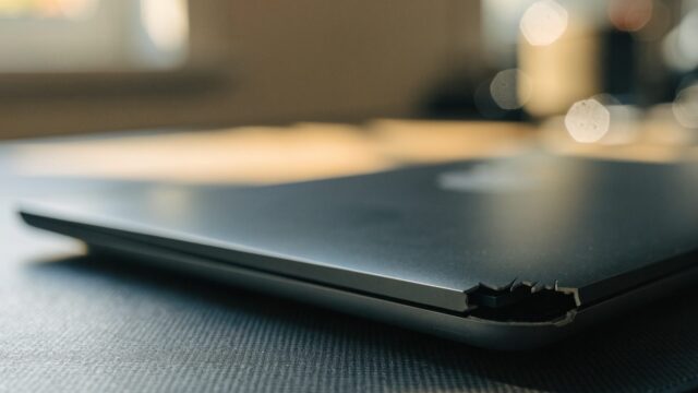 Close-up of a cracked corner on a closed graphite black laptop on a dark desk mat