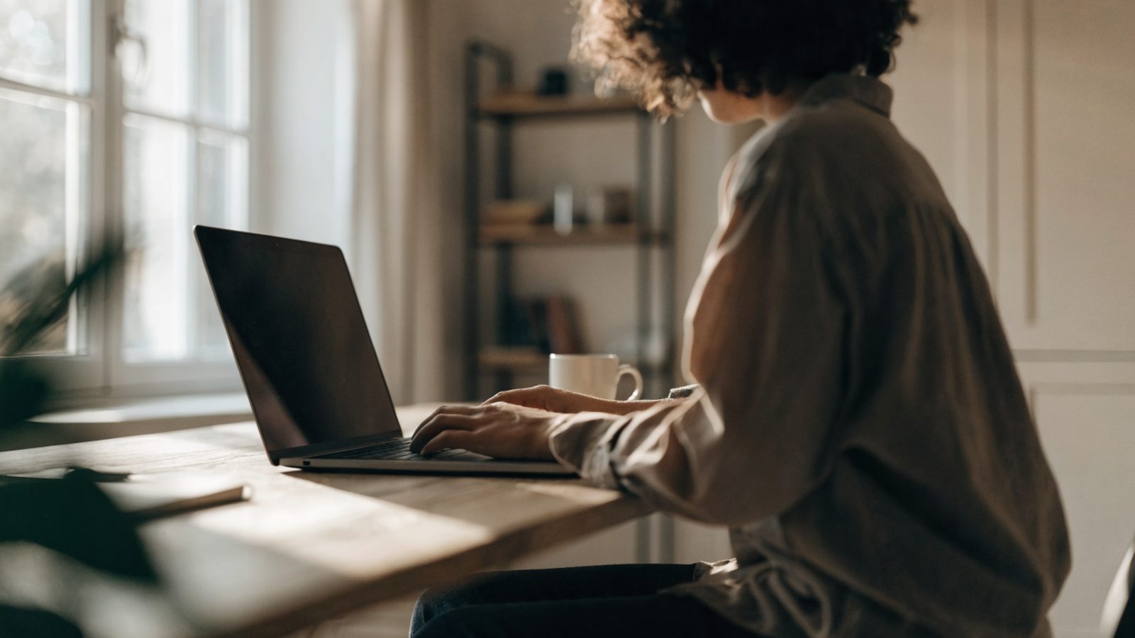 A person seen from behind working on a graphite black laptop in a bright home office