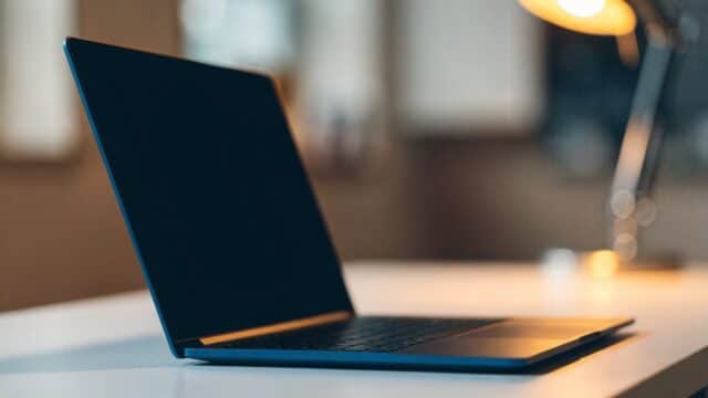 A dark blue laptop on a white desk with a completely dark blank screen