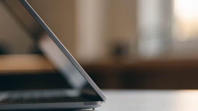 Close-up of the hinge and screen edge of a matte grey laptop on a white desk