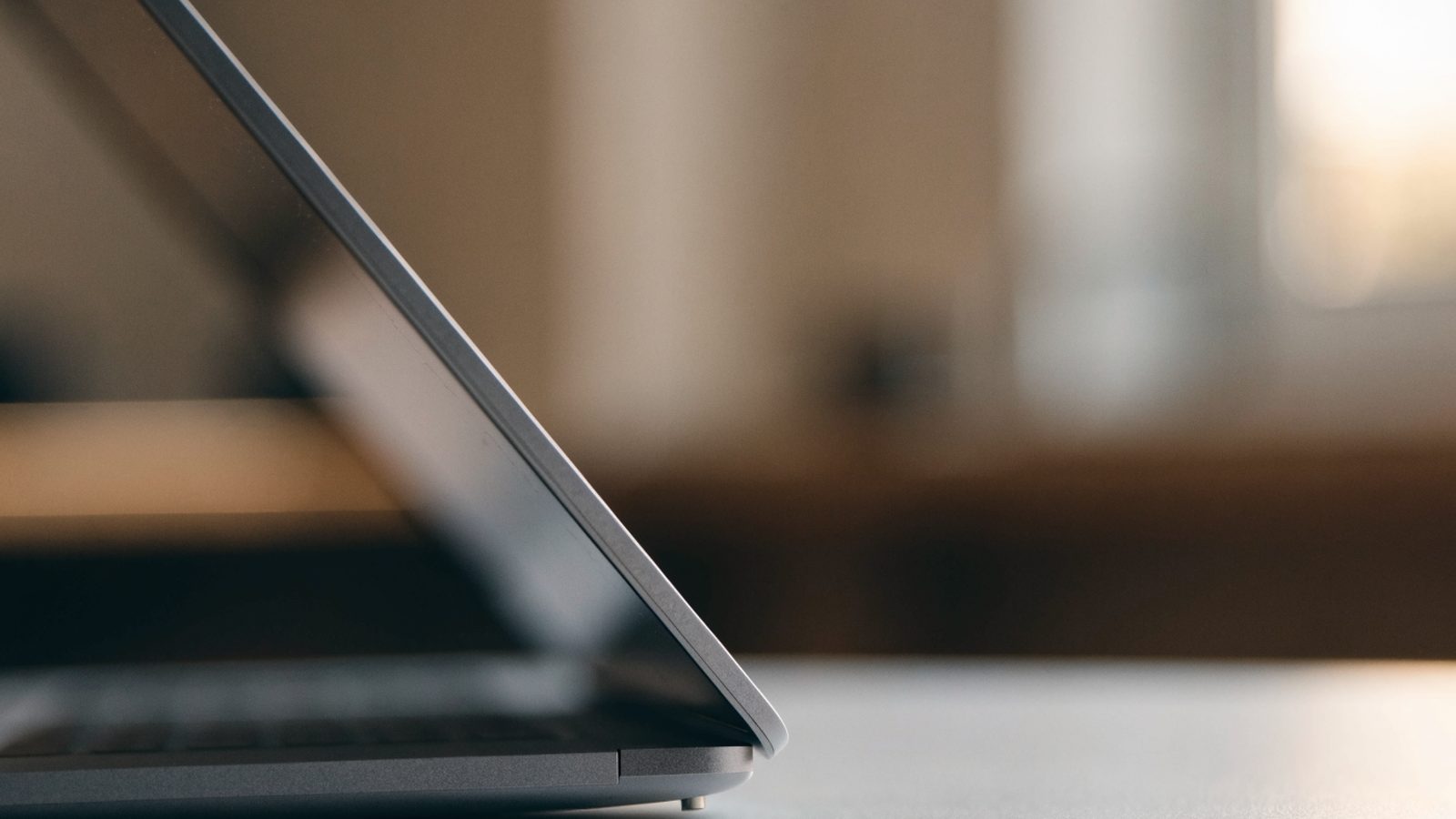 Close-up of the hinge and screen edge of a matte grey laptop on a white desk