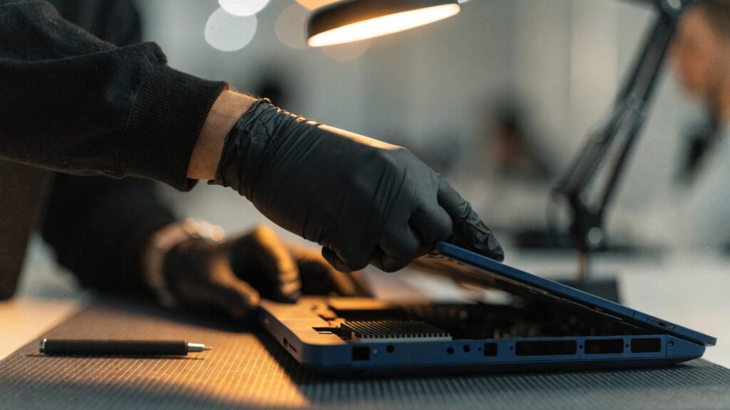 A technician lifting the bottom cover off a dark blue laptop on an anti-static mat