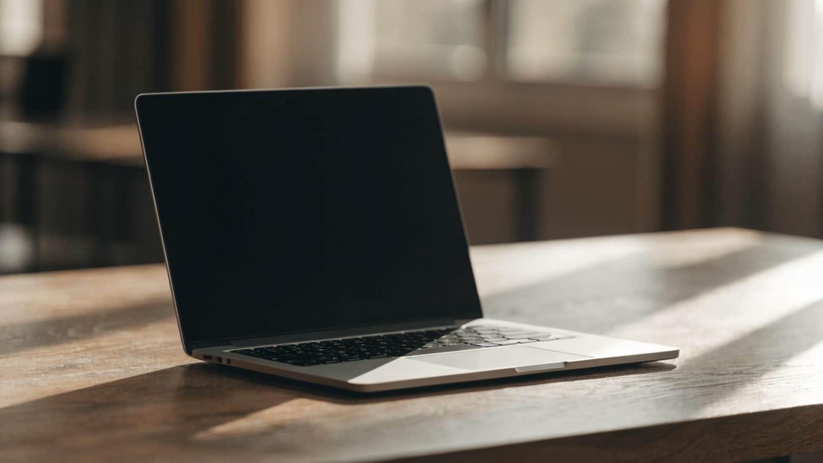 A silver laptop on a wooden desk with a completely dark blank screen