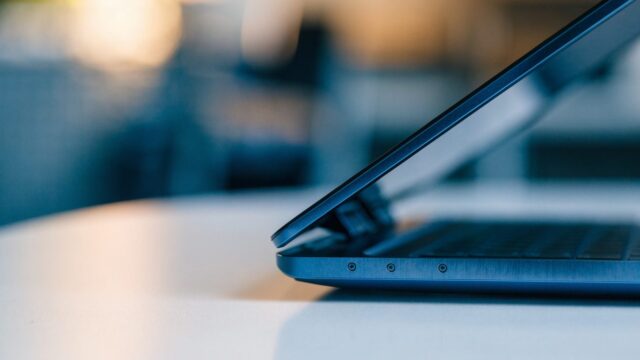 Close-up of the hinge and screen edge of a dark blue laptop on a white desk
