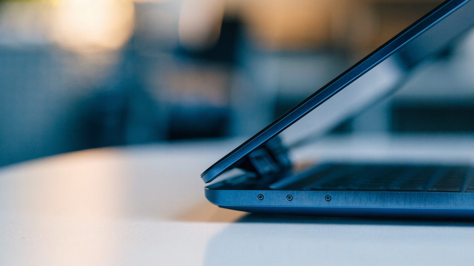 Close-up of the hinge and screen edge of a dark blue laptop on a white desk