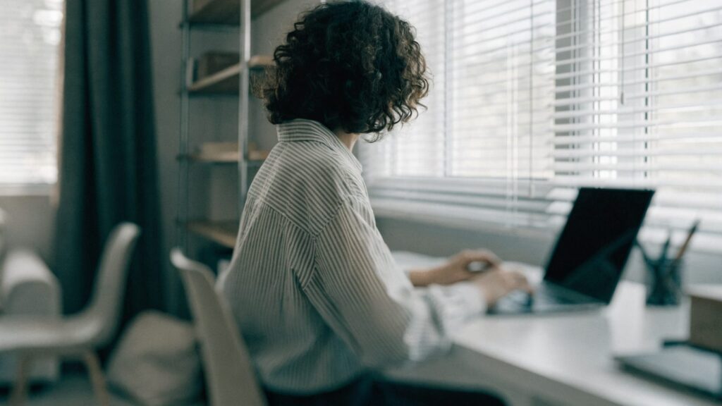 A person seen from behind working on a graphite black laptop in a bright home office