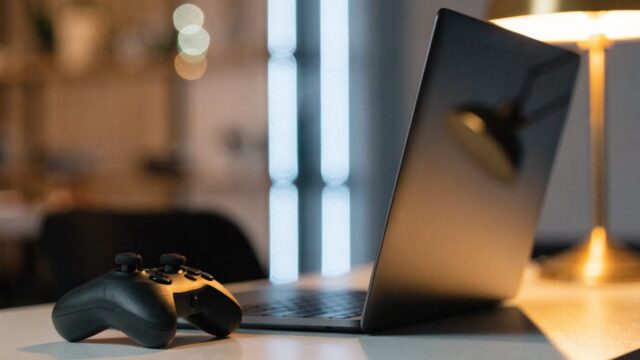 A game controller resting on a desk beside a graphite black laptop in a room with soft LED glow