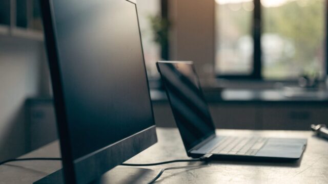 A dark blue laptop connected to a large external monitor with a blank dark screen via a cable on a workbench