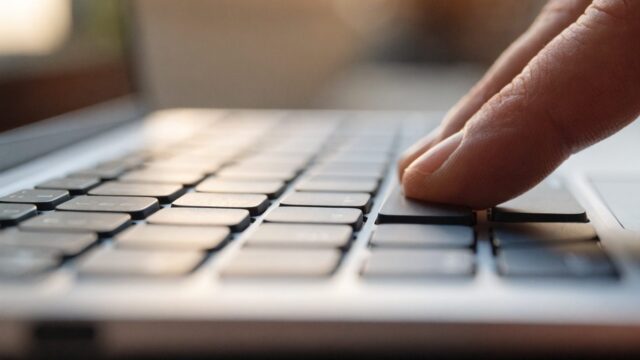 Close-up of a single key being pressed on a silver laptop keyboard