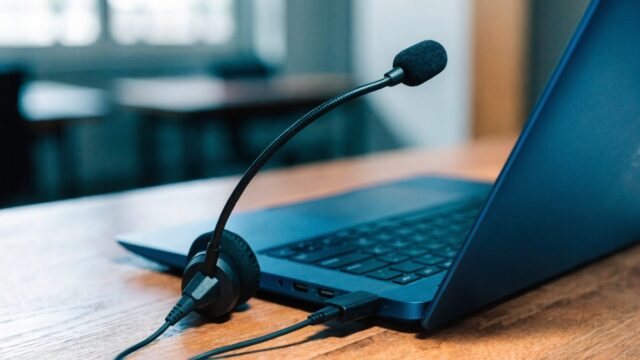 A USB headset with microphone plugged into a dark blue laptop on a wooden desk