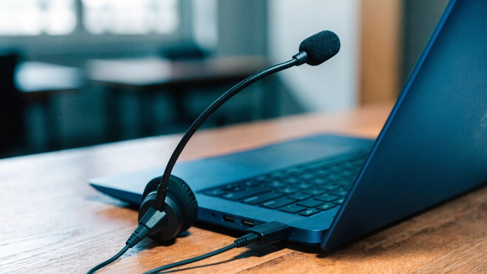 A USB headset with microphone plugged into a dark blue laptop on a wooden desk
