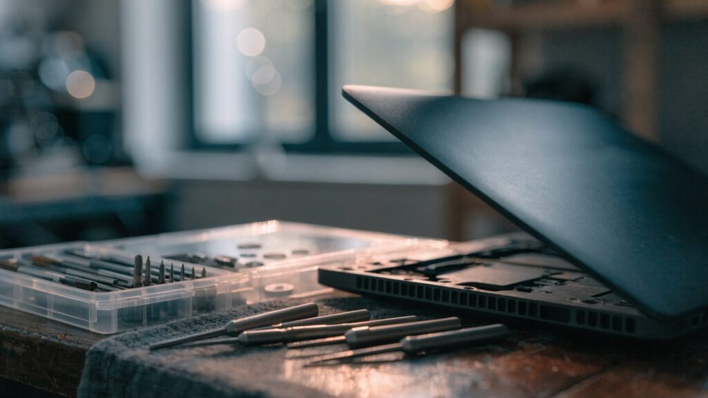 A precision screwdriver kit laid out beside a partially opened graphite black laptop on a workbench