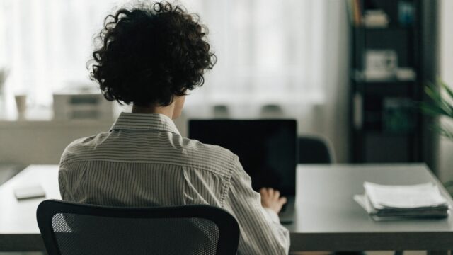 A person seen from behind working on a graphite black laptop in a bright home office