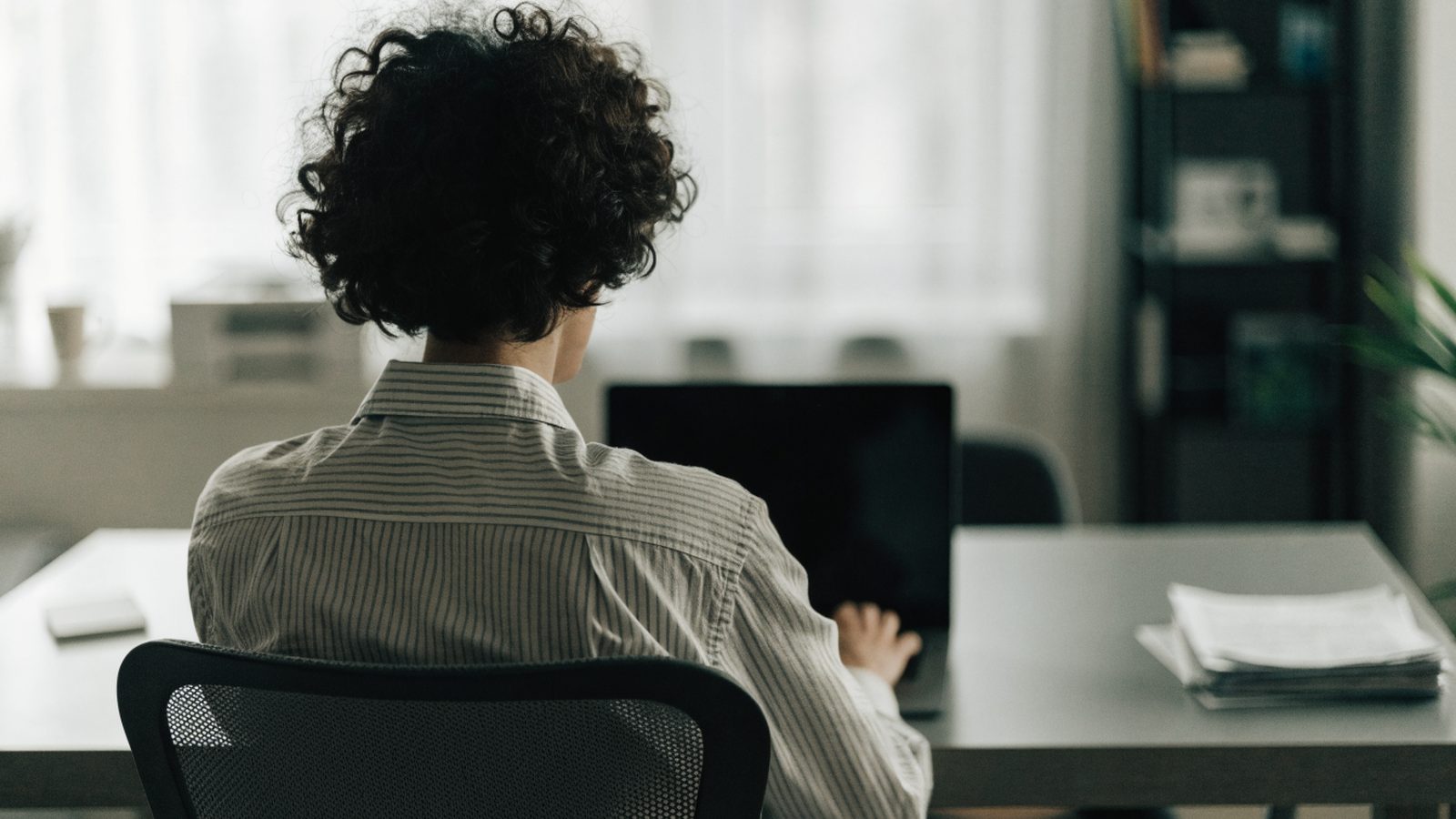 A person seen from behind working on a graphite black laptop in a bright home office