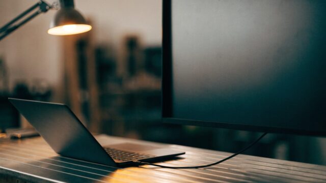 A graphite black laptop connected to a large external monitor with a blank dark screen via a cable on a workbe
