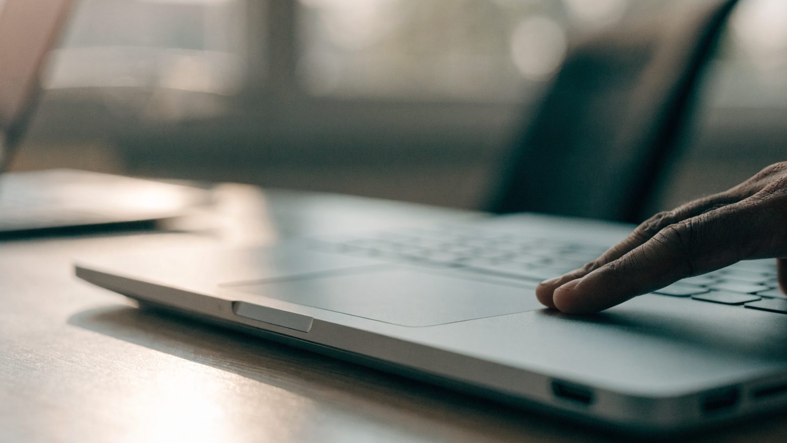 A finger gliding on the touchpad of a matte grey laptop on an office desk