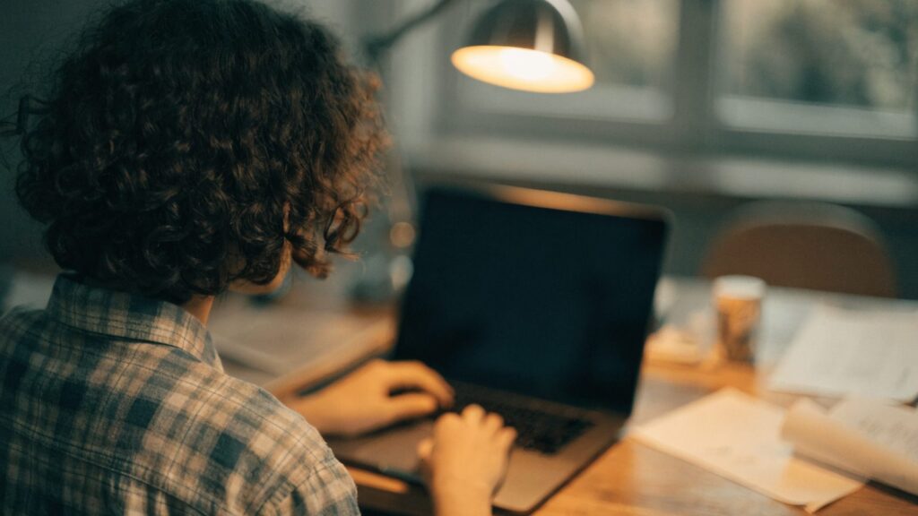 A teenager seen from behind doing homework on a graphite black laptop at a desk
