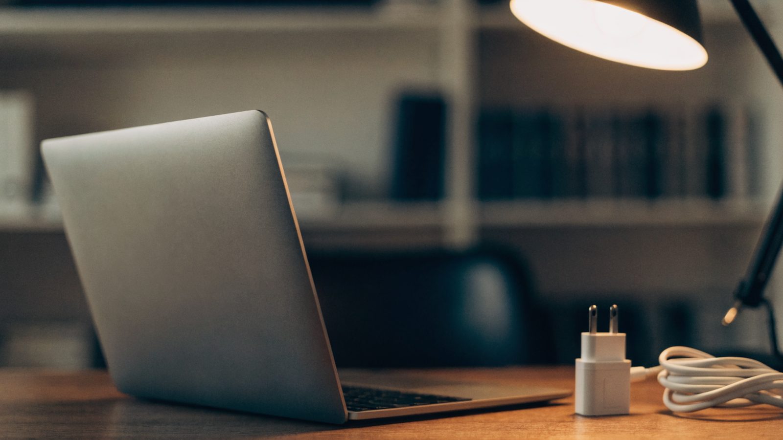 A matte grey laptop on an office desk next to a compact white power adapter with its cable neatly coiled