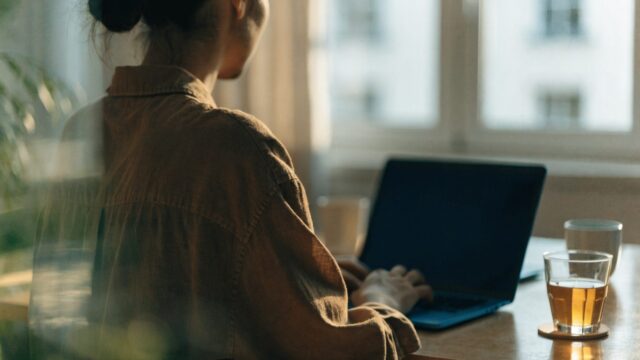 A person seen from behind working on a dark blue laptop in a bright home office