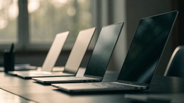 Several modern laptops lined up in a row on a dark desk mat
