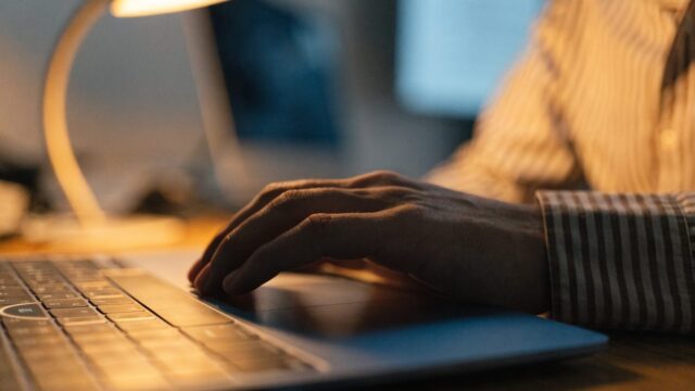 A hand resting on a dark blue laptop trackpad