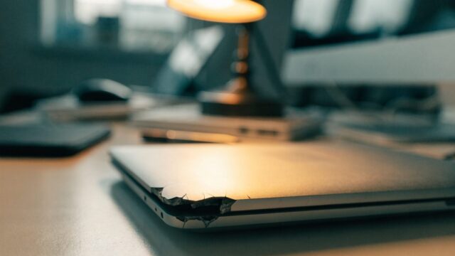 Close-up of a cracked corner on a closed silver laptop on an office desk