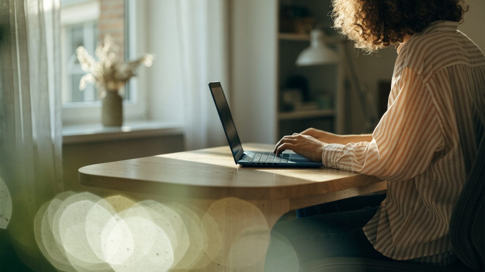 A person seen from behind working on a dark blue laptop in a bright home office