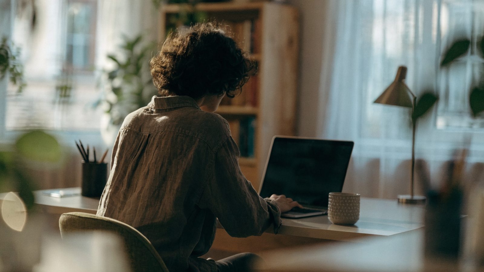 A person seen from behind working on a matte grey laptop in a bright home office