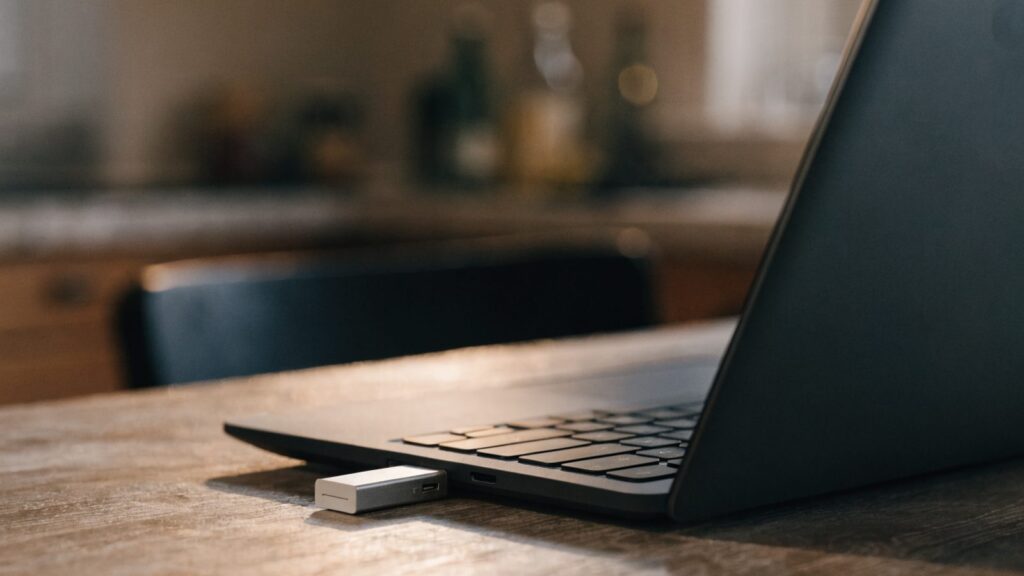 A USB flash drive plugged into the side port of a graphite black laptop on a kitchen table