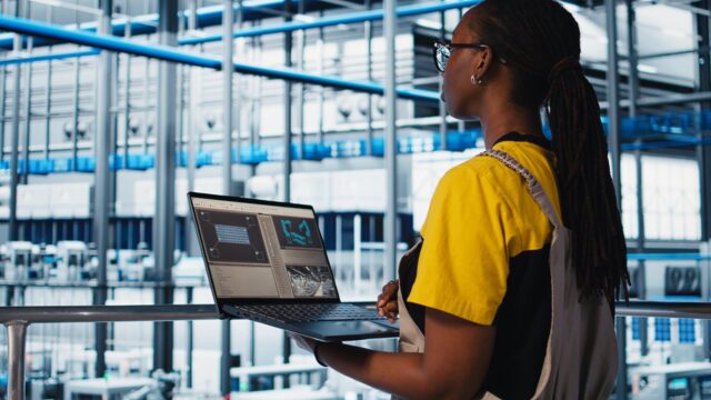 Employee using laptop in smart factory collecting and analyzing data african american woman using
