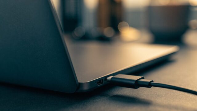 Close-up of a USB-C charger cable plugged into the side port of a graphite black laptop on a dark desk mat