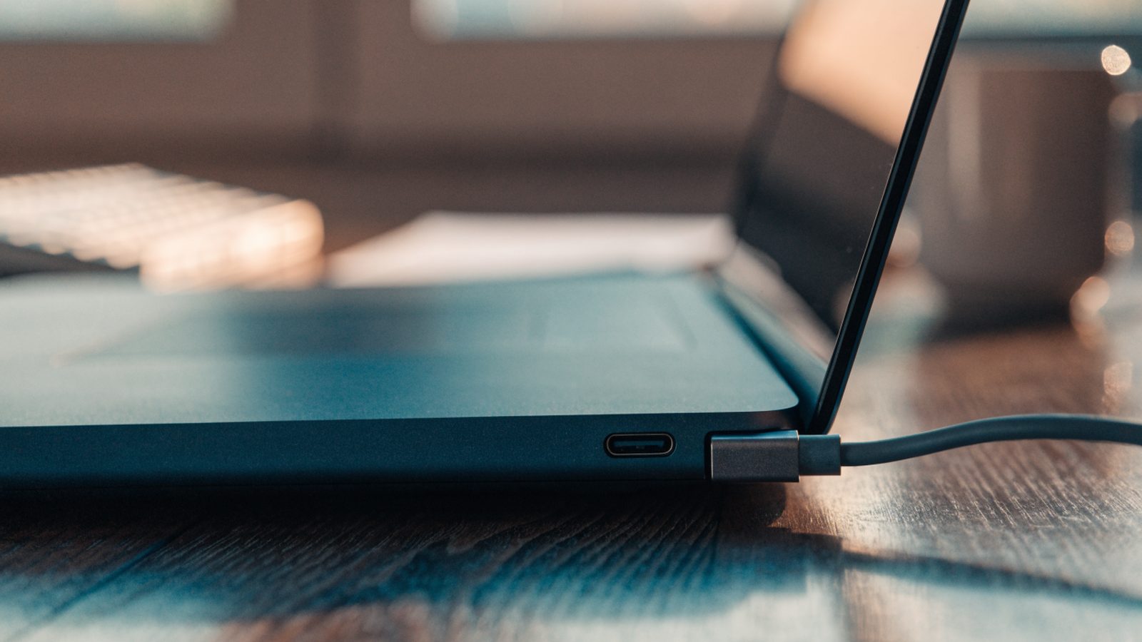 Close-up of a USB-C charger cable plugged into the side port of a dark blue laptop on an office desk