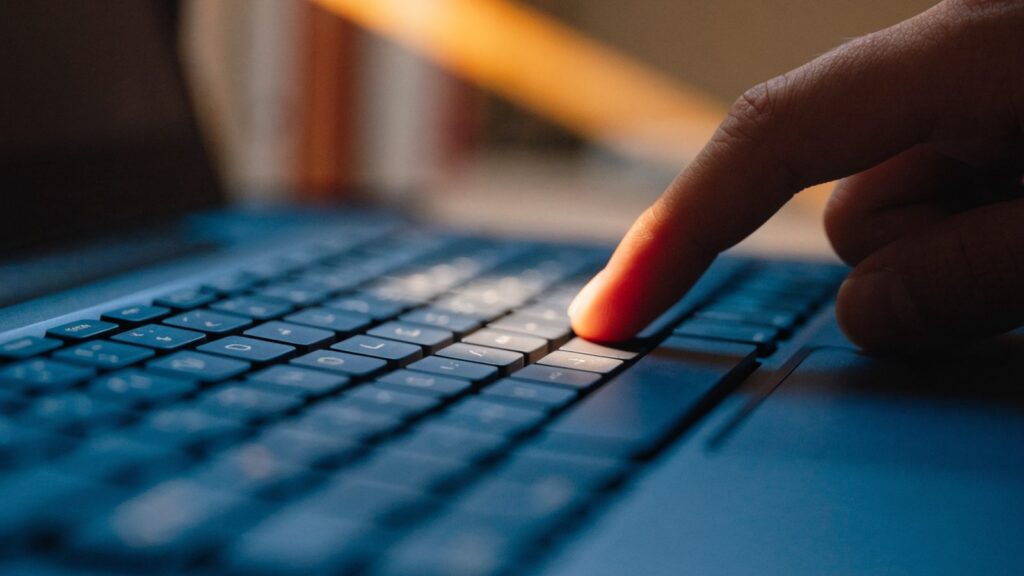 Close-up of a single key being pressed on a dark blue laptop keyboard