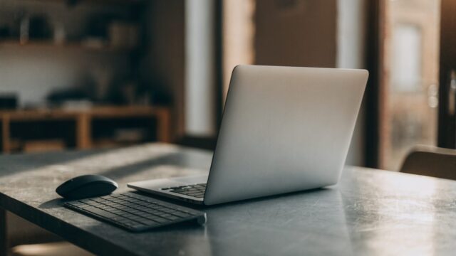 A wireless mouse and compact keyboard next to a silver laptop on a workbench