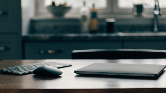 A wireless mouse and compact keyboard next to a matte grey laptop on a kitchen table
