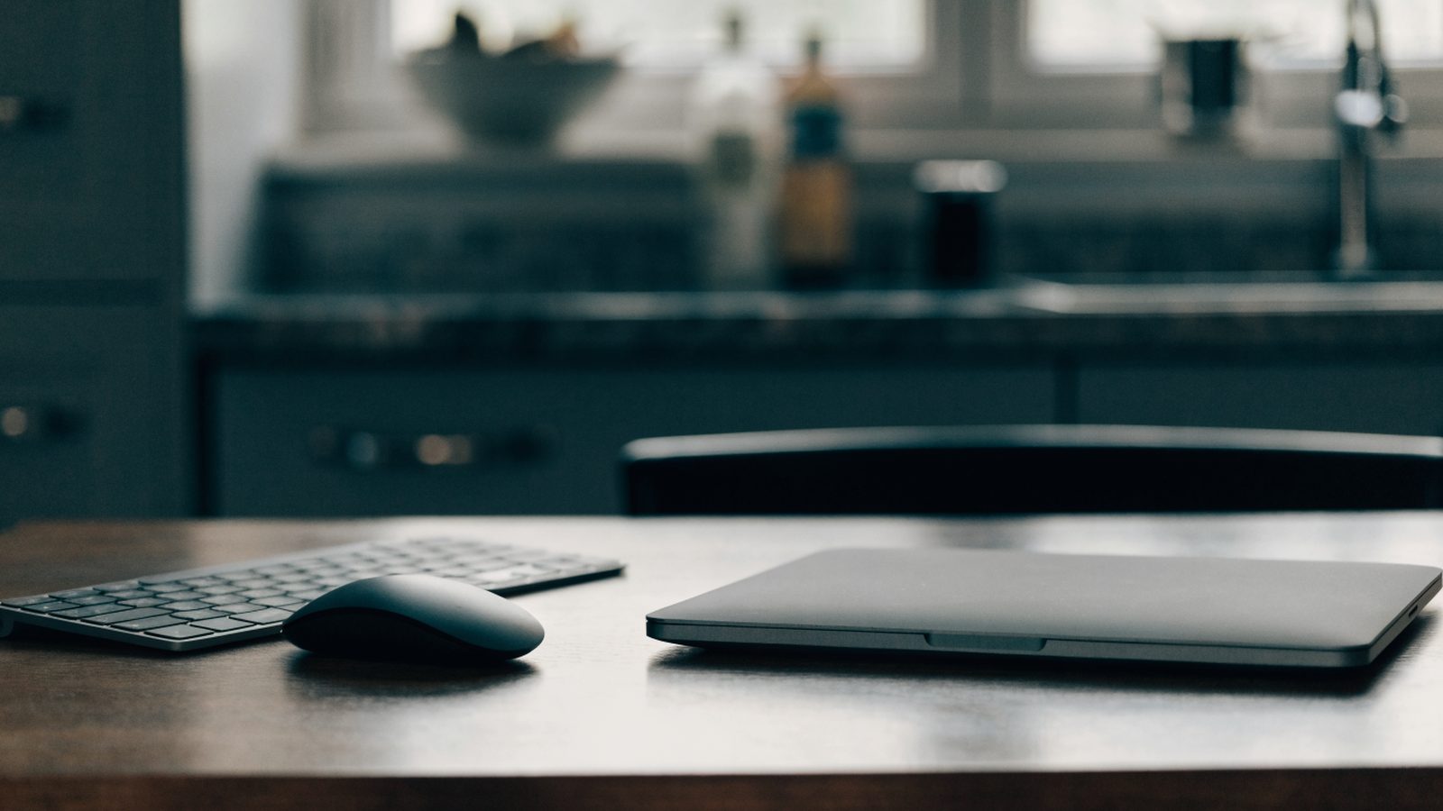 A wireless mouse and compact keyboard next to a matte grey laptop on a kitchen table