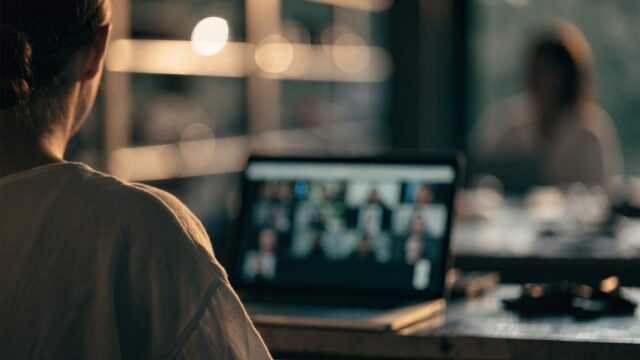 A person seen from behind on a video call on a silver laptop on a workbench