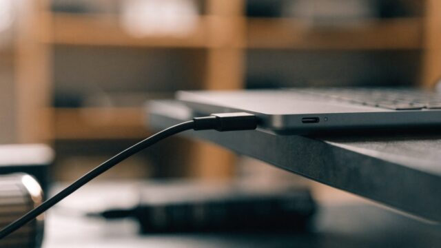 Close-up of a USB-C charger cable plugged into the side port of a matte grey laptop on a workbench