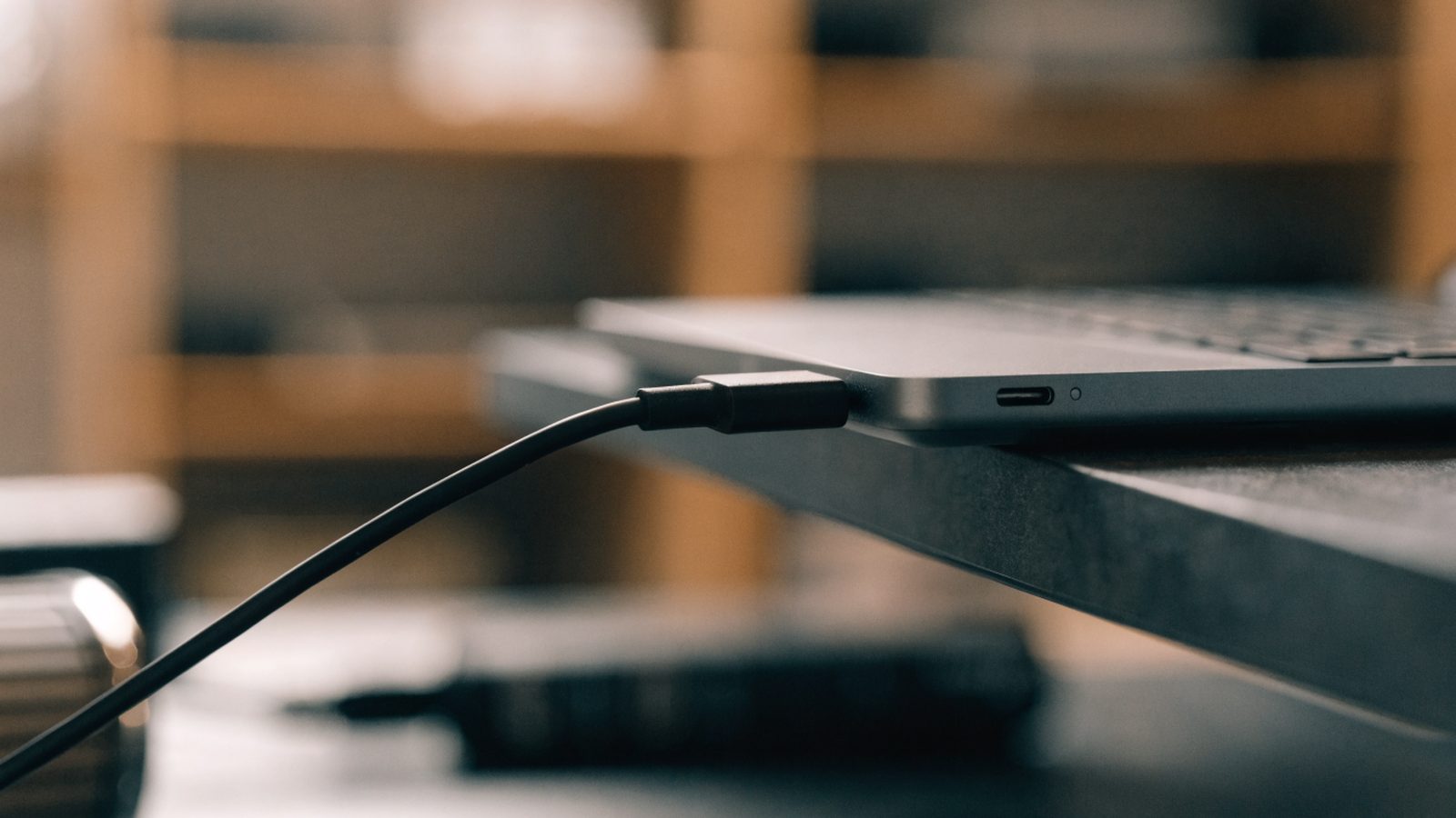 Close-up of a USB-C charger cable plugged into the side port of a matte grey laptop on a workbench