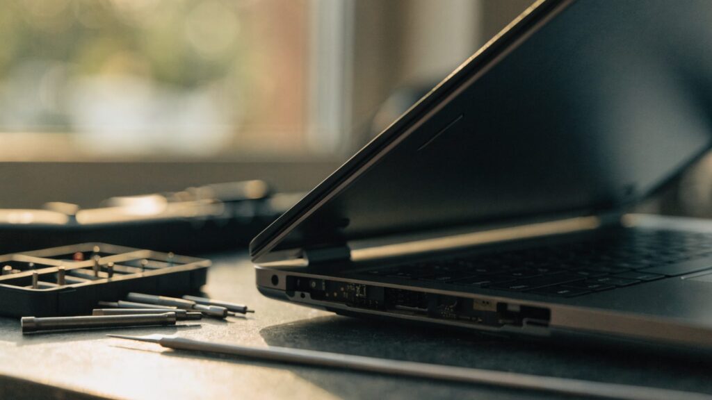 A precision screwdriver kit laid out beside a partially opened graphite black laptop on a workbench
